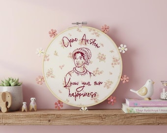May include: A circular embroidery hoop featuring a cream-colored fabric with a delicate pink floral pattern. The center displays a dark red embroidered portrait of Jane Austen with the text "Jane Austen" and "Know your own happiness" below.