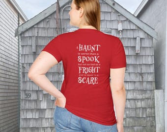 May include: A red short-sleeved t-shirt featuring white text on the back that reads: A HAUNT is worse than a SPOOK but not as bad as a FRIGHT and is equal to a SCARE. The shirt is paired with blue denim jeans, showcasing a casual and simple design.