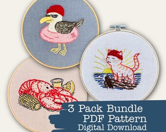 May include: Three embroidery hoops with summer-themed designs. One features a seagull in sunglasses and a floatie, another a cat watching the sunset, and the last a lobster with corn and lemon. Text reads "3 Pack Bundle PDF Pattern Digital Download."
