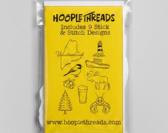 May include: A yellow rectangular package labeled Hoople Threads Includes 9 Stick & Stitch Designs. The front features black line art illustrations of a lighthouse, boat, bird, moose, lobster, pine tree, berries, and a glass, with the text Vacationland.