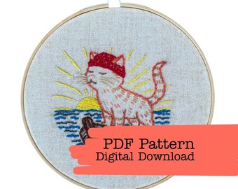 May include: Embroidery hoop featuring a cat wearing a red hat, with a sunset and ocean scene. The cat is orange and white, with yellow sun rays. The text "PDF Pattern Digital Download" is visible.