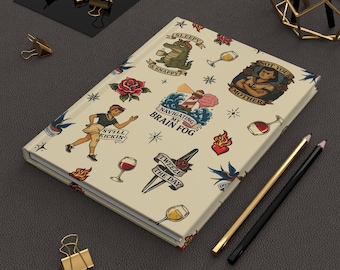 May include: A hardcover journal with a cream-colored cover featuring a repeating pattern of colorful traditional tattoo-style illustrations, including a lighthouse with the text "NAVIGATING MY BRAIN FOG," a crocodile, roses, wine glasses, and a person.