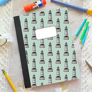 Può includere: Quaderno con sfondo azzurro chiaro e motivo di illustrazioni di fari in bianco e nero. Il quaderno ha un'etichetta bianca vuota e un dorso nero. Matite, un pennello e altri articoli di cancelleria circondano il quaderno.