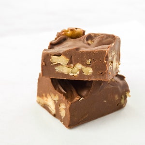 May include: Two pieces of chocolate fudge with pecans on top. The fudge is a rich brown color and the pecans are a light brown color.
