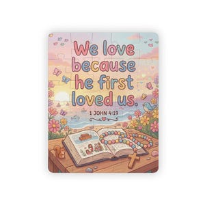 May include: A jigsaw puzzle featuring a pastel sunset landscape with flowers, butterflies, and a bird. An open book with illustrations of Noah's Ark and people sits on a wooden table with a beaded cross necklace. Text reads: We love because he first loved us. 1 JOHN 4:19.