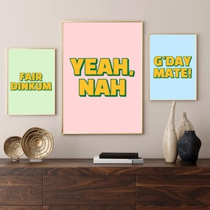 Peut inclure: Trois impressions d'art encadrées avec des cadres dorés et des fonds colorés. Les impressions présentent les phrases "FAIR DINKUM", "YEAH, NAH" et "G'DAY MATE!" en texte jaune et vert. Les impressions sont affichées sur une surface en bois foncé.