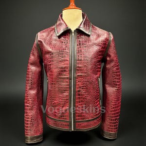 Pode incluir: Casaco de couro vermelho com textura de pele de crocodilo. O casaco tem fecho de correr, gola e acabamentos castanhos. O casaco é exibido num manequim.