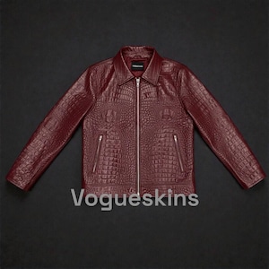 May include: A burgundy leather jacket with a crocodile skin texture. The jacket has a collared neckline, a zipper closure, and two side pockets. The text "Vogueskins" is displayed on the front.