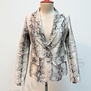 May include: A snakeskin-patterned blazer in shades of gray and white, displayed on a mannequin. The jacket features a notched lapel, two front pockets, and a single-button closure. The overall design is a classic tailored style.