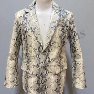 Puede incluir: Blazer con estampado de piel de serpiente en tonos beige, gris y negro. La chaqueta presenta solapa de muesca, dos bolsillos delanteros y cierre de un botón. El blazer se exhibe en un maniquí.