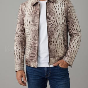 May include: A beige and brown jacket featuring a textured crocodile skin pattern, a classic collar, and a full-length front zipper. The garment includes long sleeves with zippered cuffs and two vertical zippered pockets on the front torso area.
