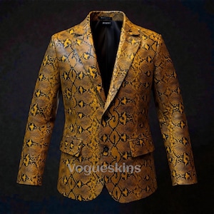 Peut inclure: Un blazer à motif peau de serpent jaune et noir, avec une fermeture à deux boutons et des revers crantés. La veste a deux poches avant et une doublure noire. Le texte "Vogueskins" est visible en bas à droite.