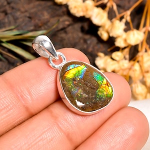 May include: A silver pendant with an oval-shaped ammolite gemstone. The ammolite displays a mosaic of iridescent colors, including green, yellow, and blue, set in a polished silver bezel. The pendant has a loop for a chain.