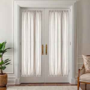 May include: Two white interior doors with matching sheer curtains. The curtains are gathered at the top and bottom, creating a soft, textured look. The doors have brass-colored handles and are set in a white frame. A potted plant and a decorative chair are visible.