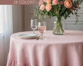 May include: A round, light pink linen tablecloth with a ruffled edge. The tablecloth is set on a table with a vase of pink roses, two wine glasses, and a plate. Text on the image reads "CUSTOM LINEN TABLECLOTH 28 COLORS."