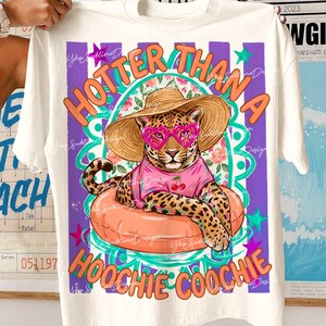 以下が含まれることがあります： クリーム色のTシャツ。ハート型のサングラスと麦わら帽子をつけたヒョウが、オレンジ色の浮き輪に乗っています。「HOTTER THAN A HOOCHIE COOCHIE」の文字はオレンジとターコイズブルーです。