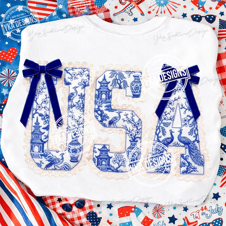 May include: White sweatshirt featuring the word "USA" in blue and white chinoiserie-style lettering. Each letter is trimmed with cream lace and embellished with a blue velvet bow. The design incorporates pagodas, vases, and birds.