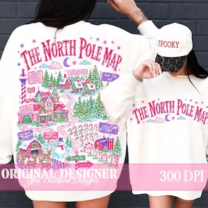 May include: A white sweatshirt and matching baseball cap featuring a colorful graphic of The North Pole Map. The design includes a candy cane path, a snowman, reindeer, and buildings labeled Claus Residence and Elf Village. The cap says SPOOKY.