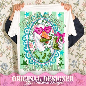 May include: White t-shirt featuring a cartoon goose wearing heart-shaped sunglasses and a pickle-patterned shirt, holding a pickle and a jar of pickles. The shirt has the text "Pickles and Goose, Salty & Silly."