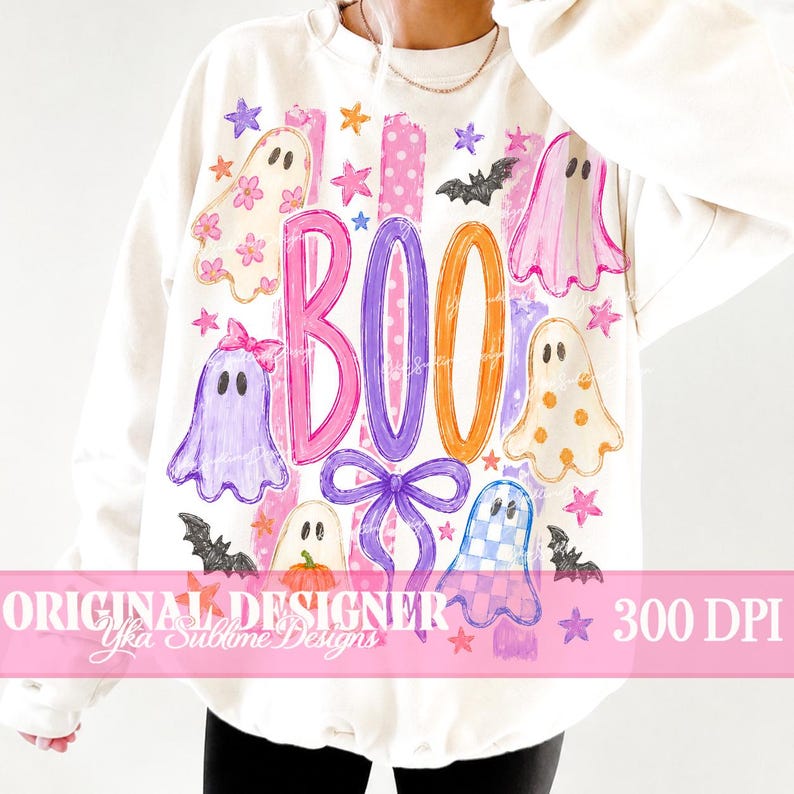 May include: A cream-colored long-sleeve sweatshirt featuring a graphic print with the text BOO, colorful ghosts, bats, stars, and a bow. The ghosts have various patterns including flowers, polka dots, and checkers in pink, purple, and orange hues.