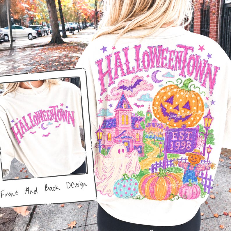 May include: A cream-colored t-shirt featuring a graphic design with the text HALLOWEENTOWN in pink. The back design displays a colorful illustration of a haunted house, a large jack-o'-lantern, a ghost, a scarecrow, and a sign reading EST. 1998.