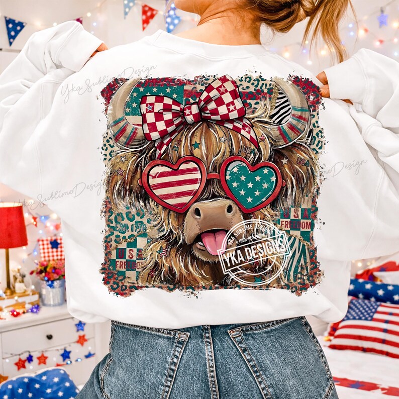 Puede incluir: Sudadera blanca con un dise&ntilde;o de vaca de las Tierras Altas con elementos patri&oacute;ticos. La vaca lleva gafas de sol en forma de coraz&oacute;n con patrones de la bandera estadounidense y un lazo a cuadros rojo y blanco. El dise&ntilde;o incluye estrellas, rayas y la palabra "FREEDOM".