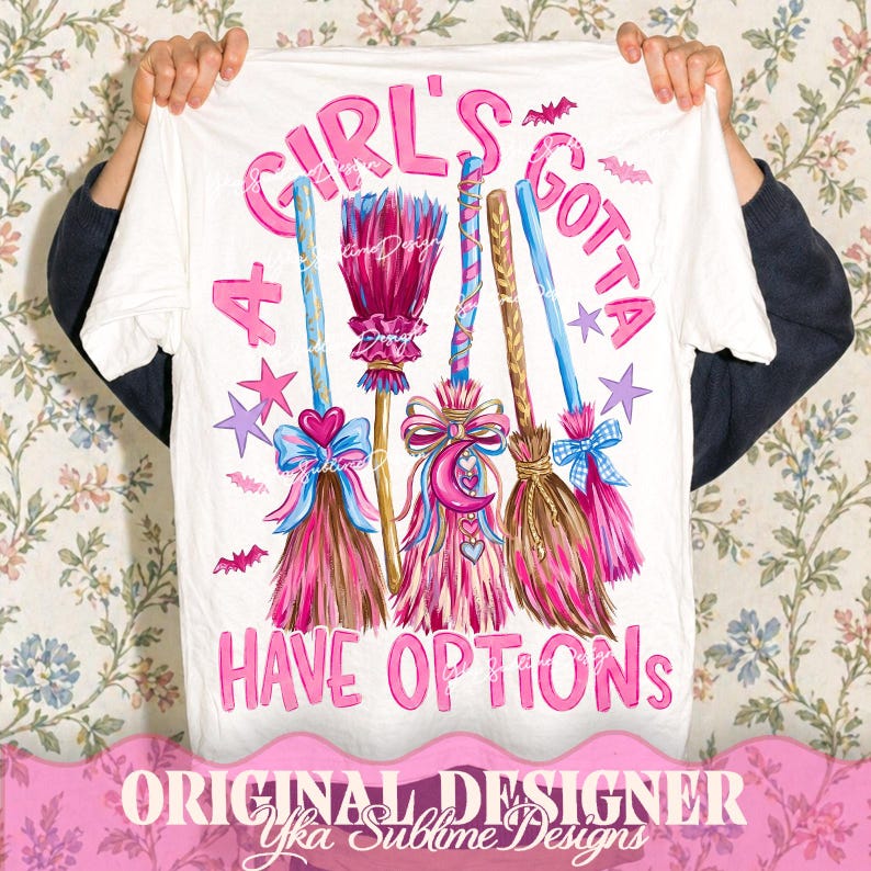 May include: A white t-shirt featuring a graphic print of four stylized brooms in shades of pink, blue, and brown. The text "A GIRL'S GOTTA HAVE OPTIONS" is printed in pink letters, accompanied by small purple stars and pink bat illustrations.