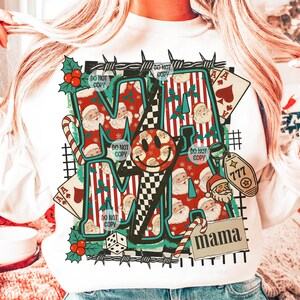May include: White sweatshirt with a graphic design featuring the word "MAMA" and a smiley face. The design incorporates Santa Claus, playing cards, candy canes, and the number 777. The words "DO NOT COPY" are also visible.