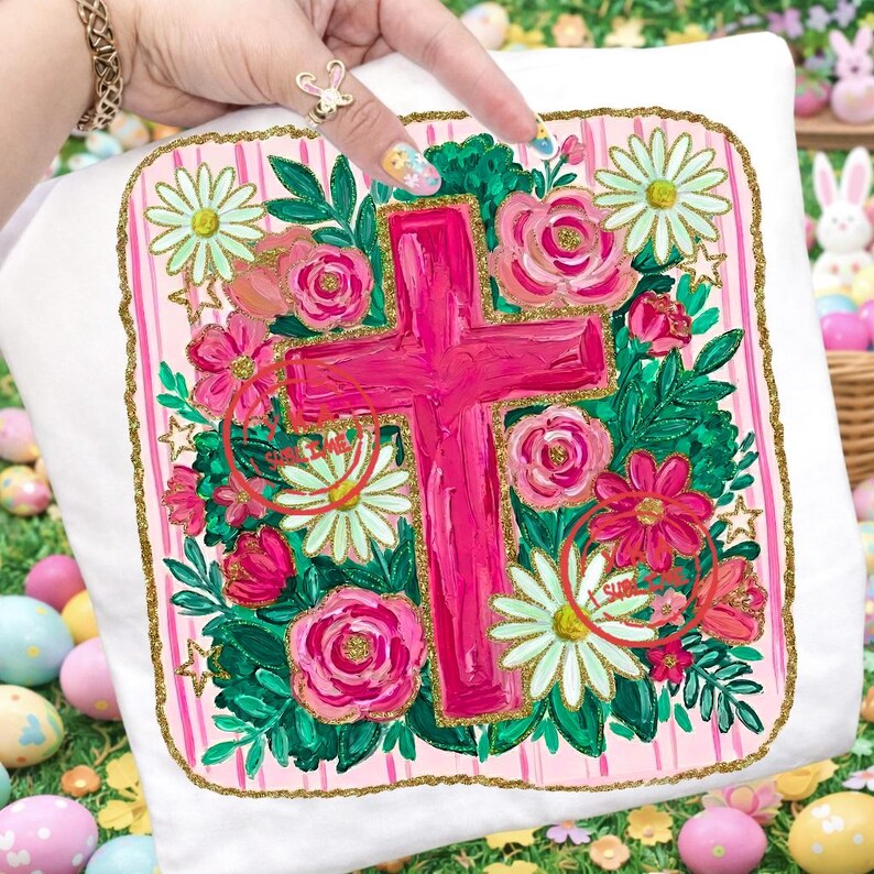 Peut inclure: Coussin blanc avec un motif de croix rose entour&eacute; de fleurs. La croix est peinte en rose vif, et les fleurs comprennent des roses roses, des marguerites et d'autres fleurs. Le coussin a une bordure dor&eacute;e scintillante et des rayures roses.