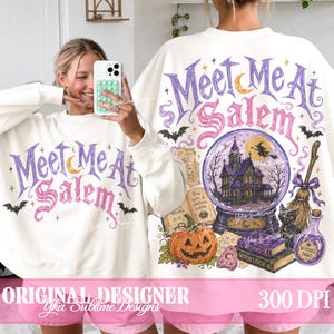 May include: A white long-sleeve sweatshirt featuring a graphic print with the text Meet Me At Salem in purple and pink. The design includes a crystal ball with a house, a flying witch, a jack-o'-lantern, a black cat, a broom, and books.