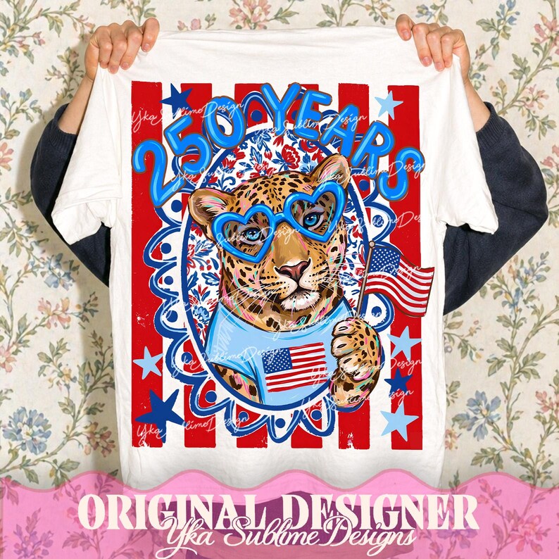 Op de afbeelding: Wit t-shirt met een luipaard met hartvormige blauwe zonnebril en een blauw shirt met een Amerikaans vlagontwerp. Het shirt heeft de tekst "250 YEARS" in blauw, met rode en blauwe sterren en strepen. De woorden "Original Designer" zijn ook zichtbaar.