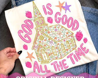 May include: A white t-shirt featuring a graphic of a church building with a floral pattern, surrounded by pink strawberries and orange and purple stars. The text "GOD IS GOOD ALL THE TIME" is printed in pink bubble letters around the church illustration.