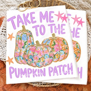 Może przedstawiać: Biały t-shirt z fioletowym napisem "TAKE ME TO THE PUMPKIN PATCH" oraz trzema dyniami w kolorowy kwiatowy wzór w odcieniach różu, błękitu i pomarańczu. Projekt zawiera małe pomarańczowe i różowe gwiazdki rozmieszczone wokół tekstu.