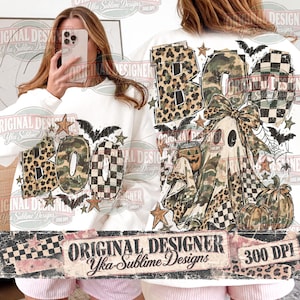 May include: A white sweatshirt featuring a graphic print of the word BOO in leopard, camouflage, and checkered patterns. The design includes a ghost wearing a bow, a pumpkin, bats, stars, and spiderwebs. The text Original Designer Yka Sublime Designs 300 DPI is visible.