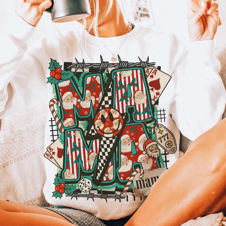 May include: White sweatshirt with a colourful graphic design. The design features the word "MAMA" in a festive font, incorporating Santa Claus imagery, candy canes, playing cards, and a smiley face. The sweatshirt has a crew neck.