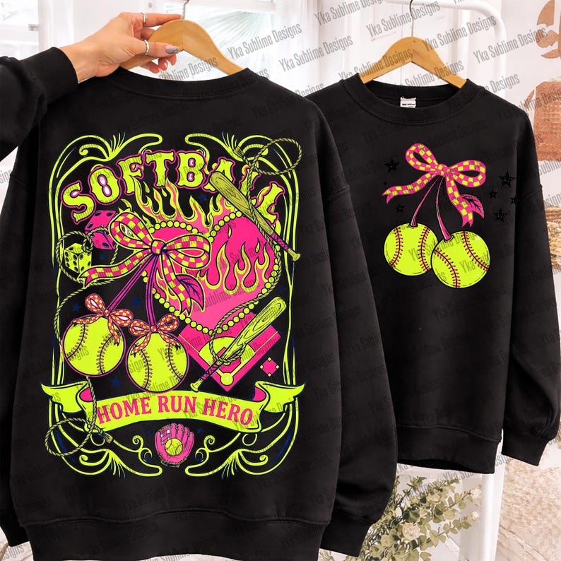 Puede incluir: Sudaderas negras con dise&ntilde;os de softbol. Una presenta un coraz&oacute;n, bates y las palabras "SOFTBALL" y "HOME RUN HERO". La otra muestra dos pelotas de softbol con un lazo. Ambas usan amarillo ne&oacute;n, rosa y negro.