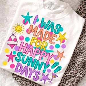 May include: White t-shirt with the text "I WAS MADE FOR HAPPY SUNNY DAYS" in colorful bubble letters. The design includes a smiling sun, bikini, starfish, dots, flip-flops, and a cocktail.