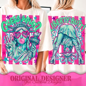 Può includere: T-shirt color crema con una grafica vivace della Statua della Libertà. La parte anteriore dice "Guess What?" e il retro dice "Liberty Butt!" in verde e rosa. La Statua della Libertà indossa occhiali da sole a forma di cuore.