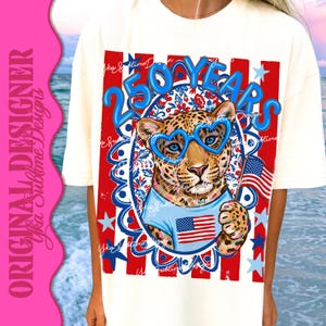 Op de afbeelding: Cr&egrave;mekleurig T-shirt met een luipaard met een blauwe hartvormige bril en een blauw shirt met een Amerikaans vlagontwerp. Het shirt heeft de tekst "250 YEARS" in blauw, met rode en blauwe patriottische sterren en strepen.