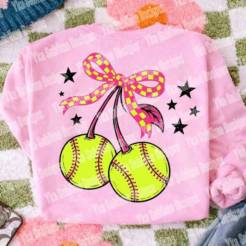 Puede incluir: Sudadera rosa con un dise&ntilde;o de softbol. El gr&aacute;fico incluye dos pelotas de softbol amarillas con costuras rojas, un lazo a cuadros rosa y amarillo, estrellas negras y el texto "Yka Sublime Designs".