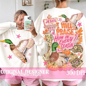 Op de afbeelding: Een wit sweatshirt met lange mouwen en een vliegende wilde eend op de voorkant. De achterkant toont een wilde eend, pompoenen, een camouflagepet, een bijbel en de tekst I Will Praise Him In Every Season en Jesus Is My Refuge.