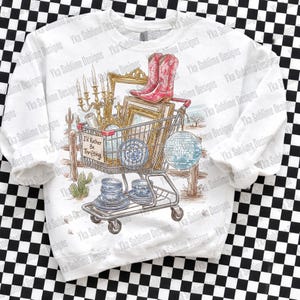 May include: White sweatshirt featuring a shopping cart filled with various vintage items, including red cowboy boots, picture frames, and blue and white china. The text "I'd Rather Be Thrifting" is on a sign.