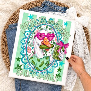 May include: A whimsical canvas print featuring a goose wearing heart-shaped sunglasses and a shirt with pickle graphics. The goose holds a pickle in its beak and a jar of pickles. Text reads "Pickles and Goose, Salty & Silly."