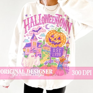 May include: A cream-colored crewneck sweatshirt featuring a vibrant, multi-colored graphic print. The design displays the text HALLOWEENTOWN above a large orange pumpkin, a haunted house, a ghost, a scarecrow, and a sign reading EST. 1998.