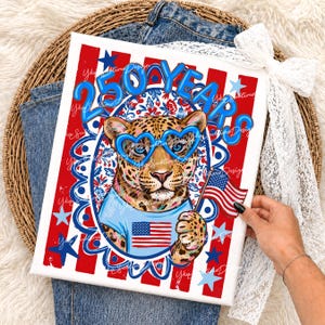 Op de afbeelding: Patriottische canvas print met een luipaard met een hartvormige bril en een shirt met de Amerikaanse vlag. De print heeft de tekst "250 YEARS" in blauw, tegen een rood-wit gestreepte achtergrond met blauwe sterren.