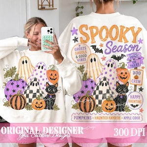 May include: A white long-sleeve sweatshirt featuring a Halloween-themed graphic with orange and purple text reading Spooky Season. The design includes illustrations of ghosts, black cats, pumpkins, bats, and stars, along with text labels.