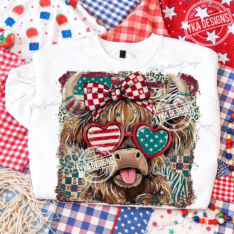 Puede incluir: Sudadera blanca con un gr&aacute;fico de una vaca de las Tierras Altas con gafas de sol en forma de coraz&oacute;n patri&oacute;ticas, un lazo y la lengua fuera. El dise&ntilde;o incorpora patrones rojos, blancos y azules y el texto "YKA DESIGNS".