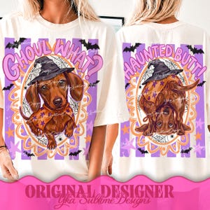 May include: An off-white t-shirt featuring two graphic illustrations of a brown dachshund wearing a witch hat and a star-patterned cape. The left graphic says GHOUL WHAT? and the right graphic says HAUNTED BUTT! with purple stripes and bats.