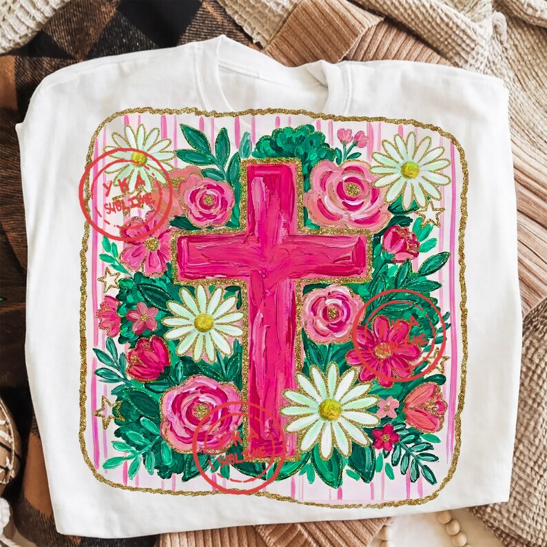 Peut inclure: T-shirt blanc avec une croix rose entour&eacute;e de fleurs et de verdure. Le motif comprend des roses roses, des marguerites blanches et une bordure dor&eacute;e scintillante. Le mot "Sublime" est visible en haut &agrave; gauche.