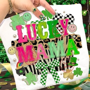 Peut inclure: T-shirt blanc avec l'inscription "LUCKY MAMA" en rose et vert, orné de trèfles, de visages souriants et d'un nœud à carreaux. Le motif comprend un fond imprimé léopard et zèbre, et un pot d'or.